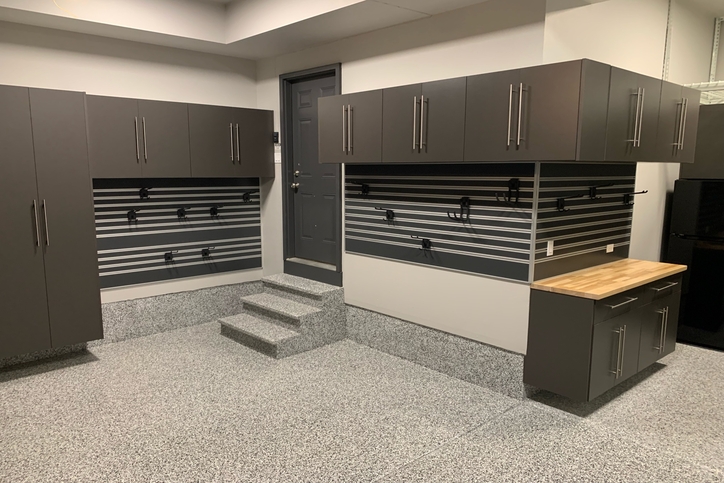Wall-mounted brown garage cabinets with slatwall storage, hanging hooks, and a butcher block work surface.