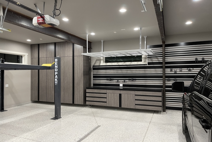 Grey wood garage cabinets with a grain finish, featuring floor-to-ceiling storage lockers, a matching workbench with drawers, and black horizontal slatwall organization.
