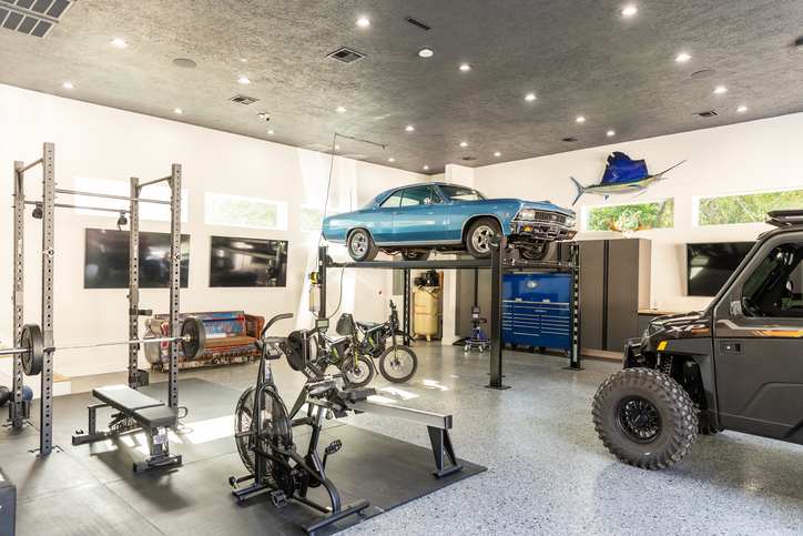 Garage with car lift, home gym, bikes, TVs, night fall flooring, charcoal cabinets, and blue workstation