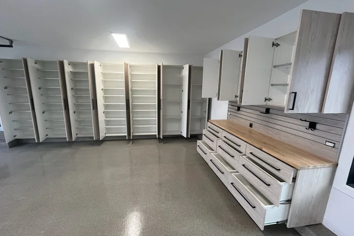 Light wood custom garage cabinets with open doors and workbench drawers.